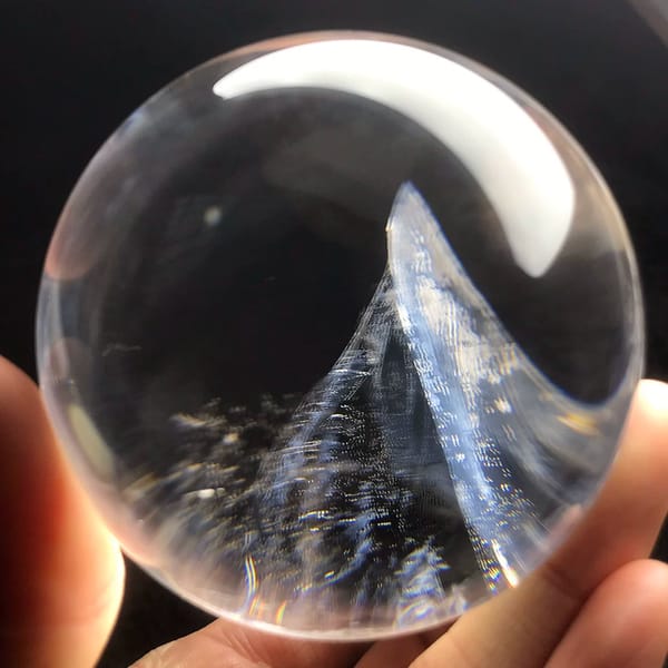 Clear quartz sphere with a blue-toned inclusion peak rising from the base