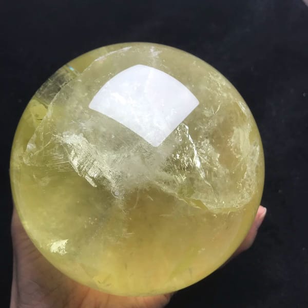 Citrine sphere with white veils and a clear yellow body in a palm