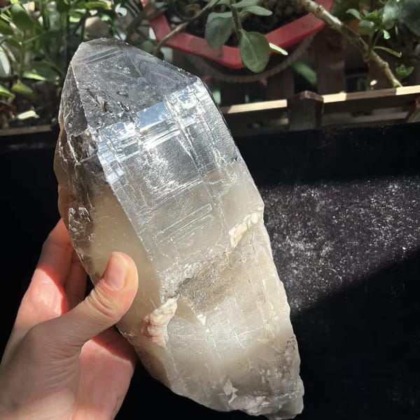 Hand holding the smoky crystal off the stand showing etched surfaces