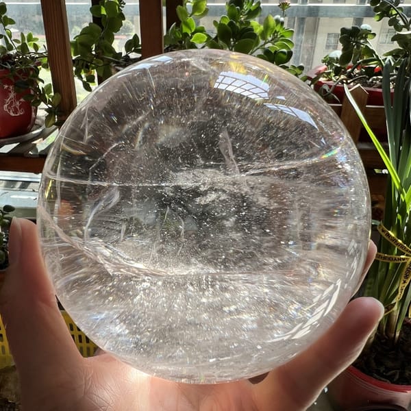 Big clear quartz sphere held up by a window with plants behind