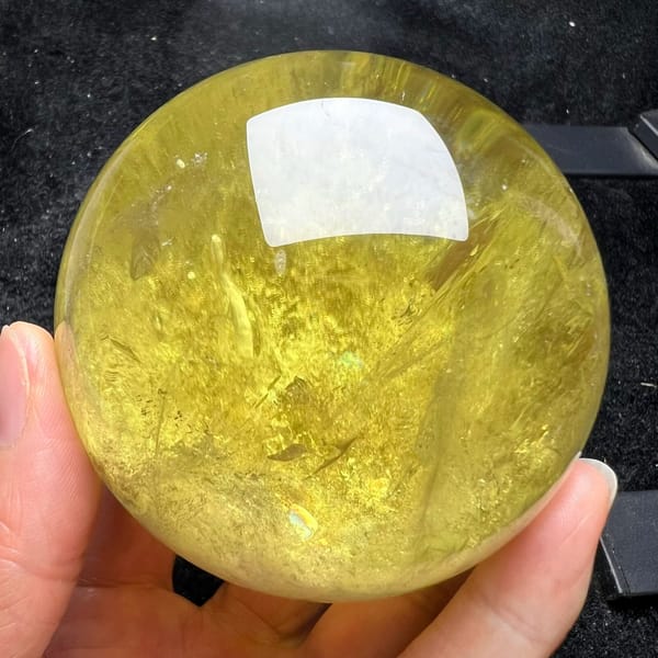 Rich golden citrine sphere held in hand with sweeping feathery veils