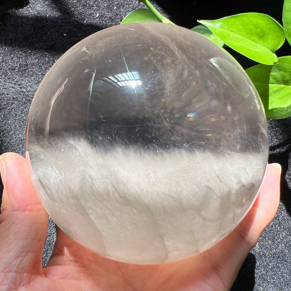 Large clear quartz sphere in hand with a level bank of white cloud below