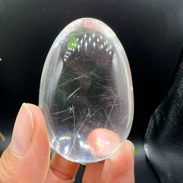 Clear rutilated quartz egg held upright with fine silvery needles inside