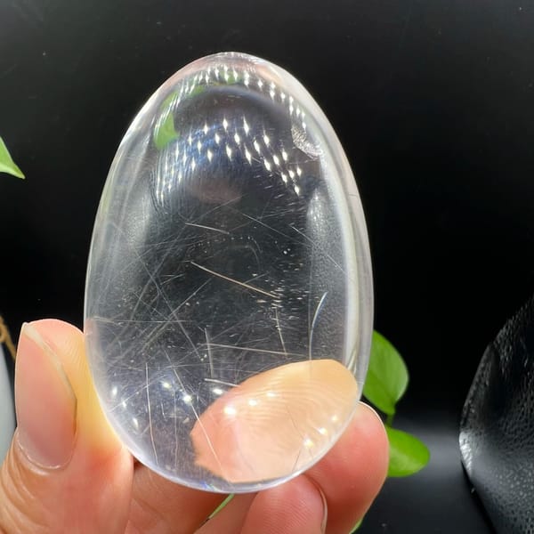 Rutilated egg held in fingertips with needles near the broad end