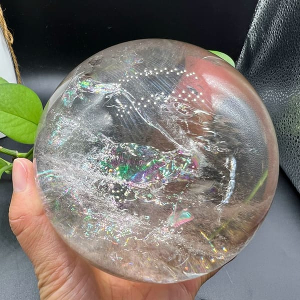 Large clear quartz sphere in hand with rainbow flashes among white veils