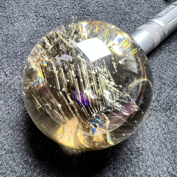 Citrine sphere on dark cloth with a torch lighting its dense curtain of silvery streaks