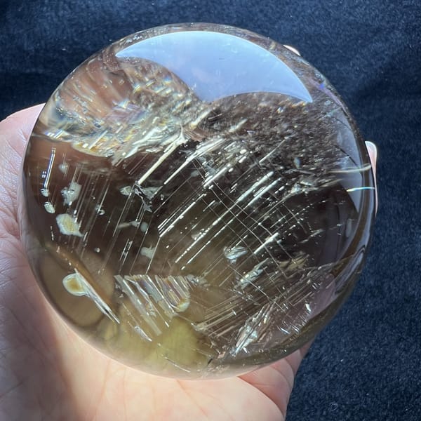 Dense crisscross net of fine silvery lines filling most of the citrine sphere