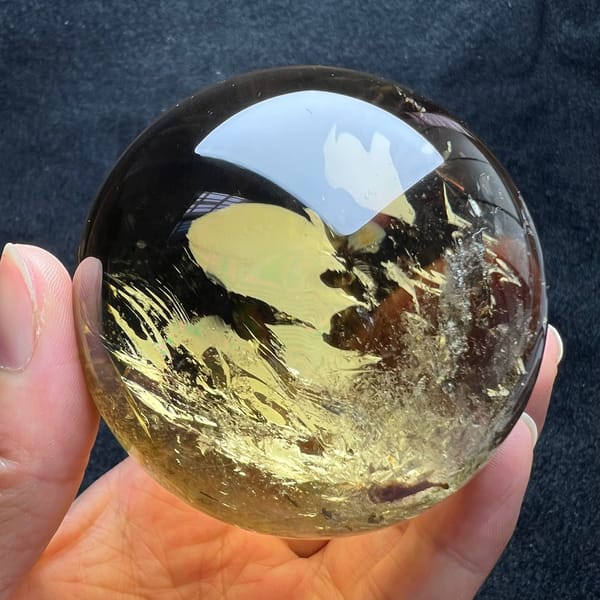 Golden citrine sphere in hand with feathery gold veils sweeping across the lower half