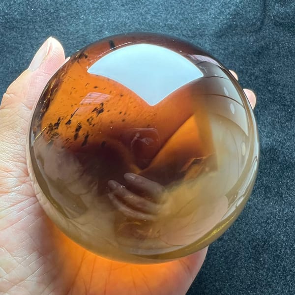 Deep amber citrine sphere with dark specks and an orange glow on the palm