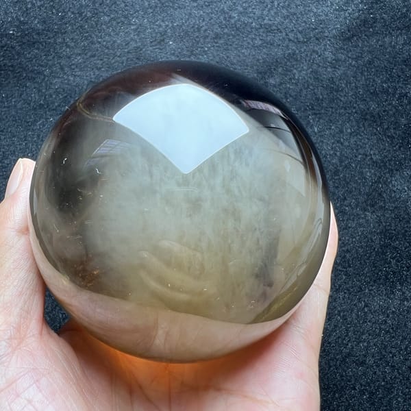 Smoky top and pale silky middle of the citrine sphere held in hand