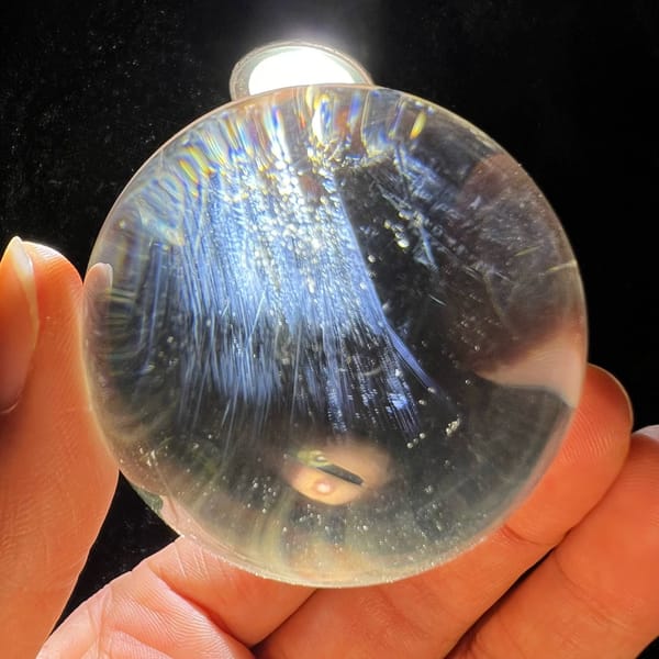 Backlit clear quartz sphere with dense blue needle sprays gathered near the top