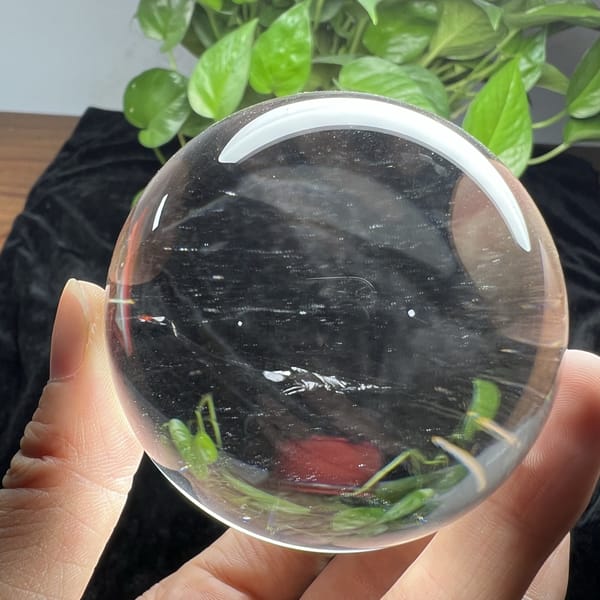 Faint drawn-silk lines and refracted greenery inside the polished sphere