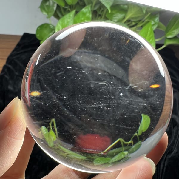 Clear quartz sphere framed by leaves with a small spark of colour at the rim