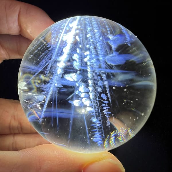 Backlit sphere with blue needles and chains of white bead-like flakes running upward