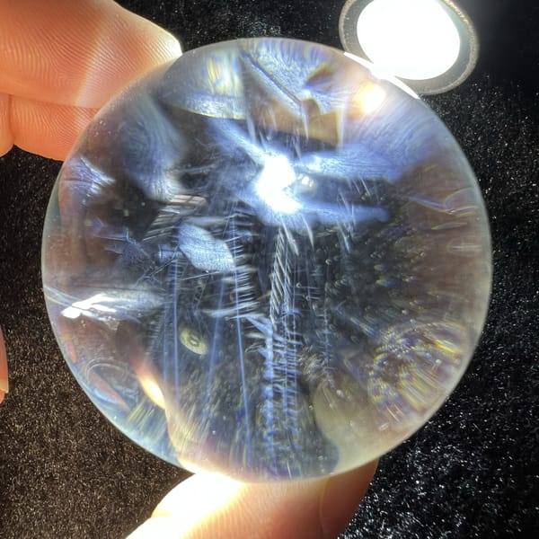 Sphere on sparkly black cloth with a torch shining through blue clouds