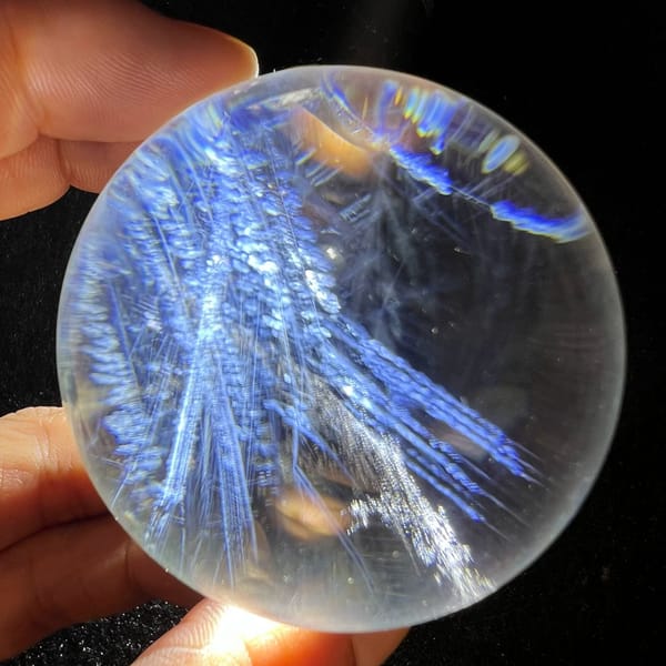 Overlapping blue feather fronds filling most of the clear quartz sphere