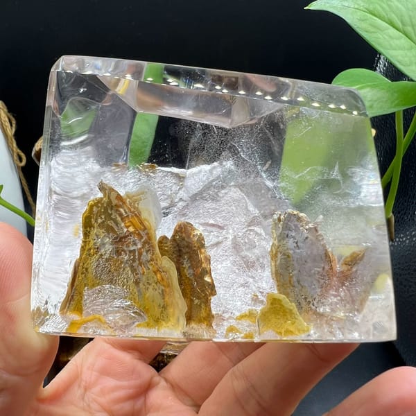 Clear quartz block in hand with golden-yellow mountain spires rising from the base