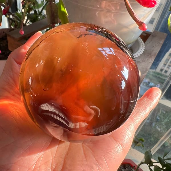 Citrine sphere glowing fiery orange in sunlight beside a window