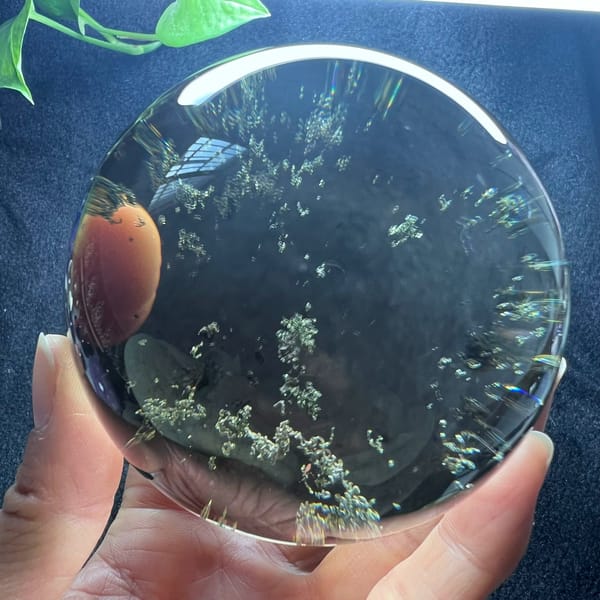 Large smoky quartz sphere with scattered green flecks and an orange reflection