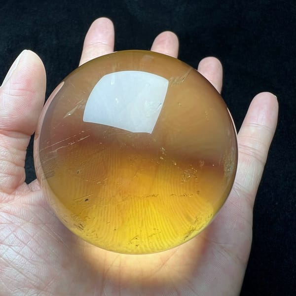 Soft yellow citrine sphere resting on an open palm in daylight