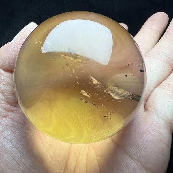 Citrine sphere on the palm with fine dark specks in the lower half