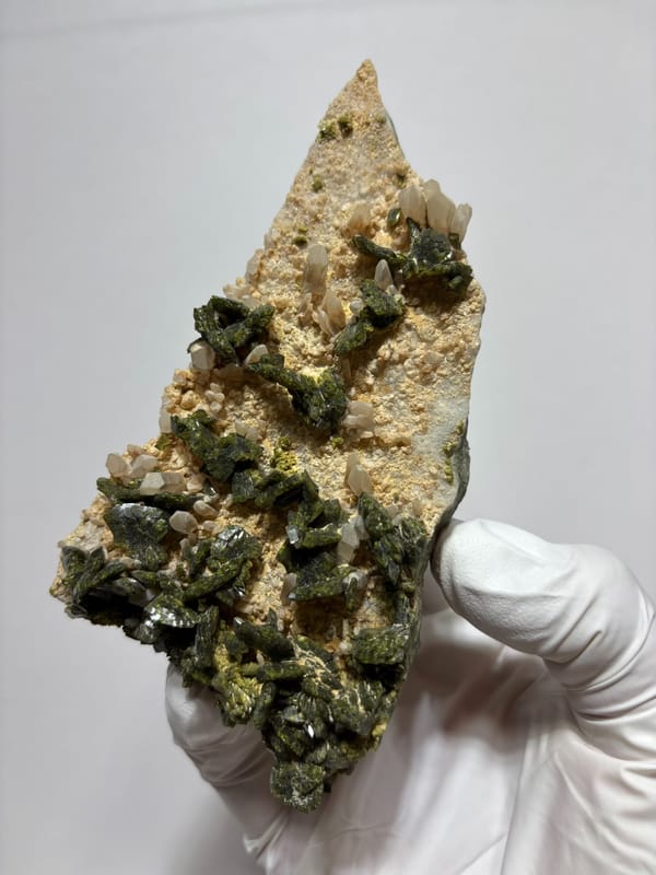 Plate of green epidote and quartz on tan matrix from Sichuan, China, held in gloved hand