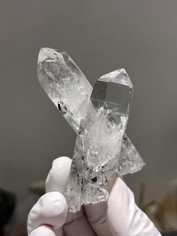 Two crossed clear quartz points with complete tips from Jinkouhe, Sichuan, China, held in gloved hand