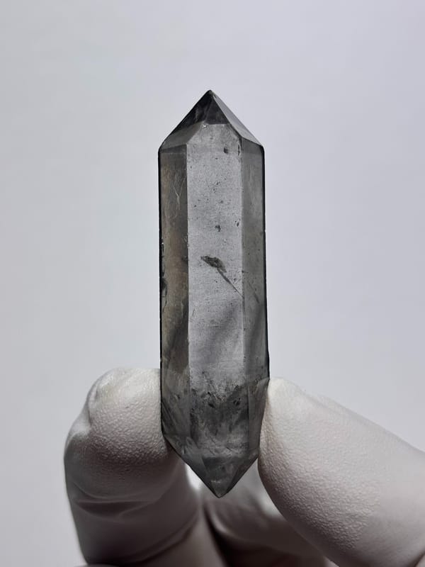 Grey double-terminated quartz wand from Yunnan, China, held in gloved hand