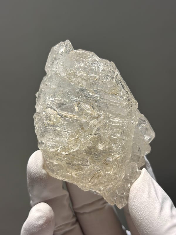 Skeletal quartz floater with sculpted faces from Jinkouhe, Sichuan, China, held in gloved hand