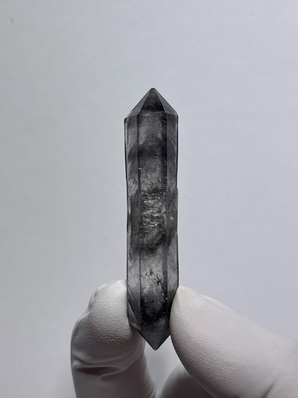 Dark smoky double-terminated quartz wand from Yunnan, China, held in gloved hand