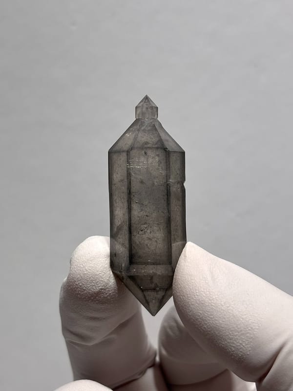 Grey sketch-pattern double-terminated quartz with sceptre tip from Yunnan, China, held in gloved hand