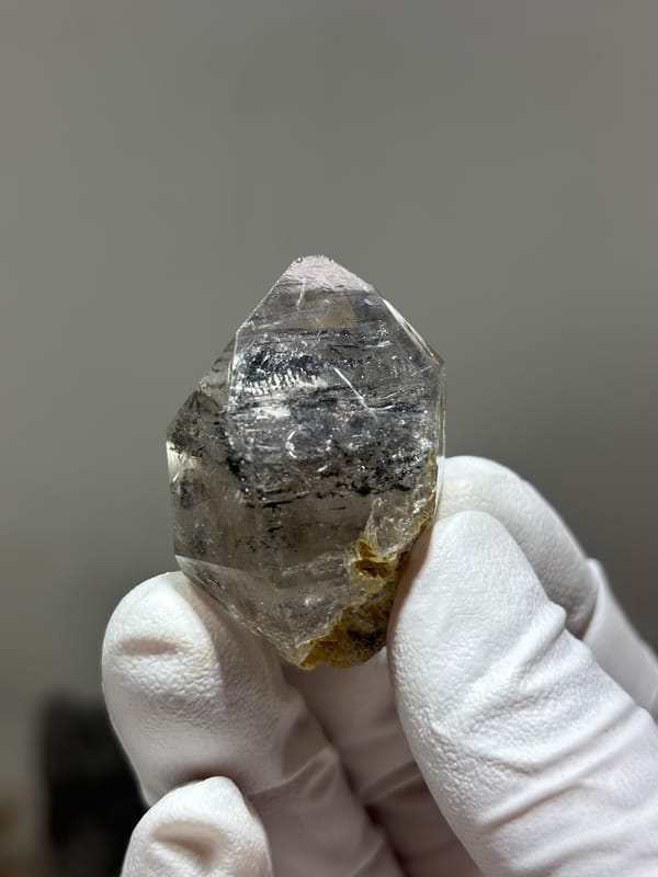 Enhydro double-terminated quartz with quicksand inclusions from Yunnan, China, held in gloved hand