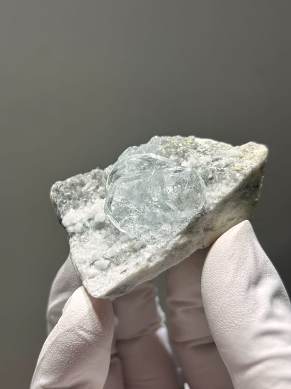 Heart-shaped aquamarine on white feldspar from Xuebaoding, Sichuan, China, held in gloved hand