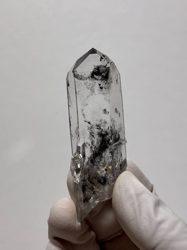 Clear quartz point with black inclusions and complete tip from Jinkouhe, Sichuan, China, held in gloved hand