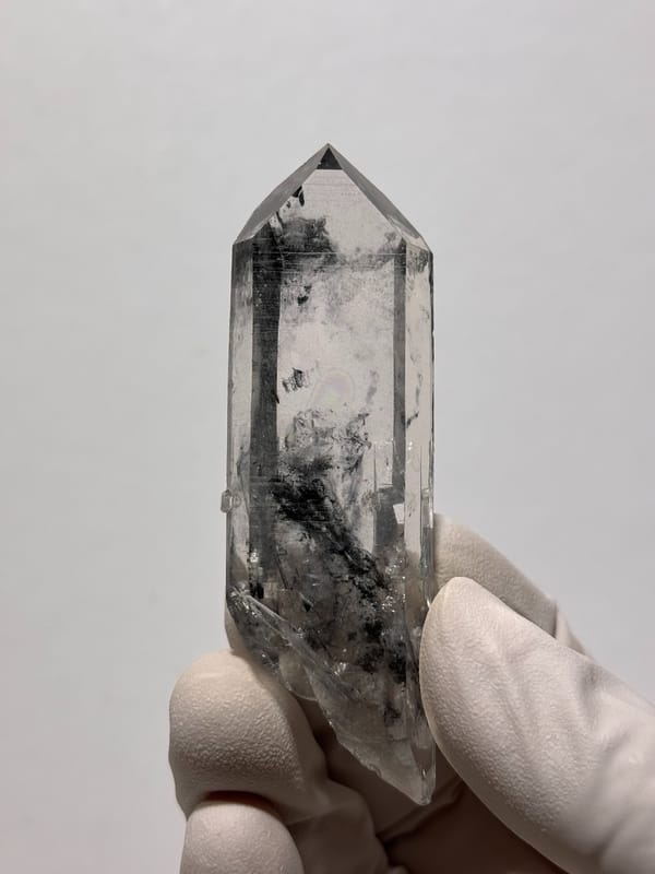 Clear quartz point with black inclusions and complete tip from Jinkouhe, Sichuan, China, close-up of the crystal faces