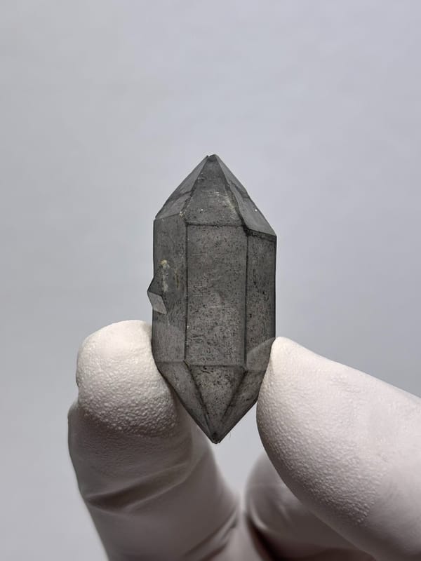 Stout grey sketch-pattern double-terminated quartz from Yunnan, China, held in gloved hand