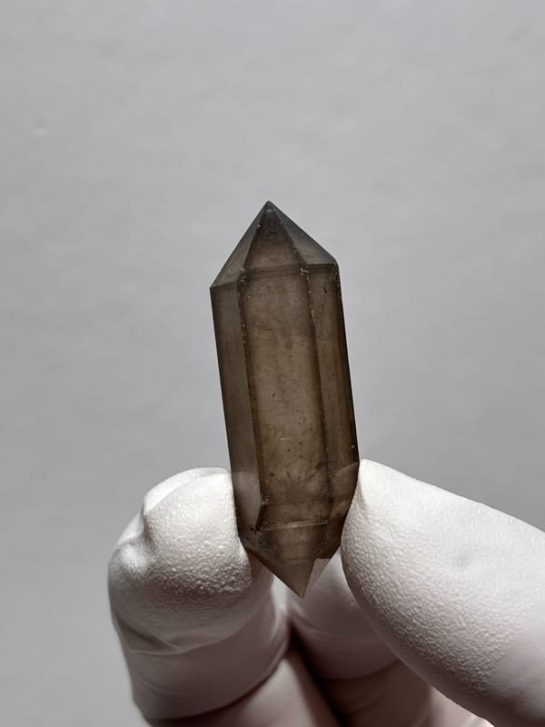 Smoky sketch-pattern double-terminated quartz from Yunnan, China, held in gloved hand