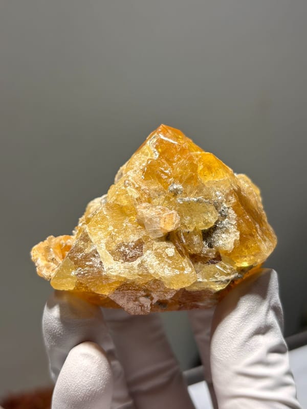 Orange scheelite crystal group from Xuebaoding, Sichuan, China, held in gloved hand