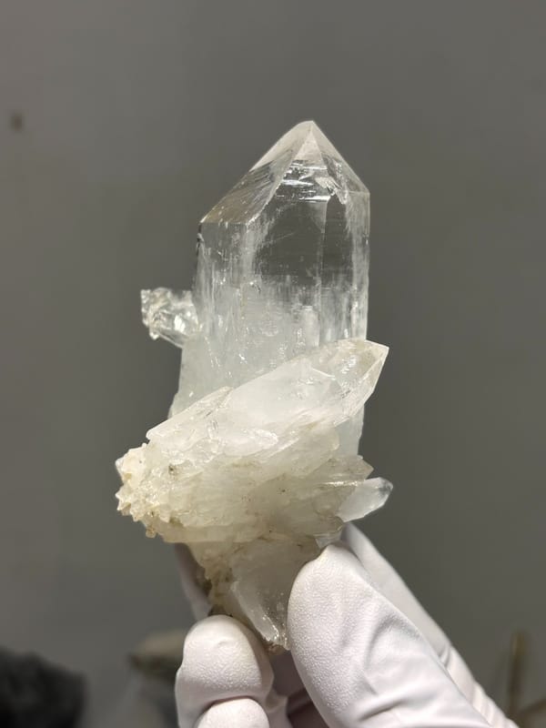 Clear quartz point on white cluster from Xuebaoding, Sichuan, China, held in gloved hand
