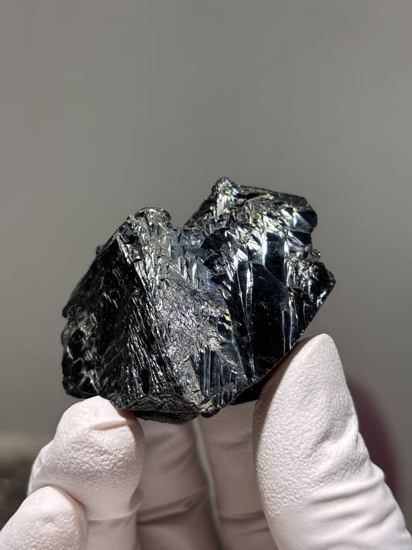 Large glossy black cassiterite crystal from Xuebaoding, Sichuan, China, held in gloved hand