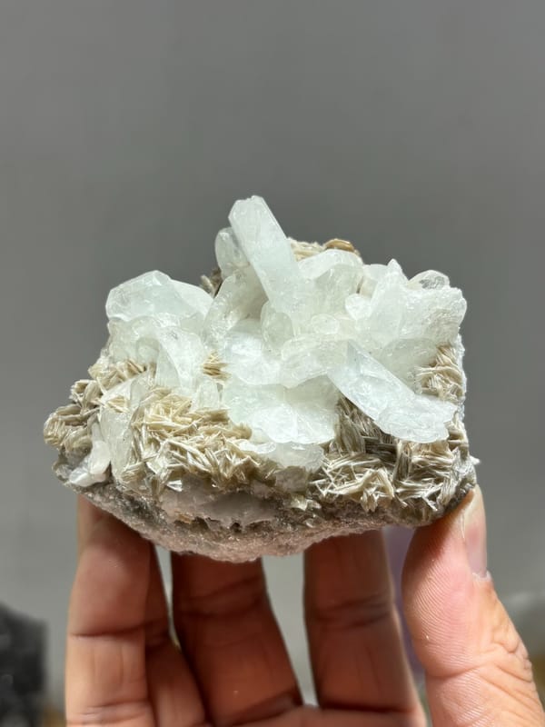 Pale aquamarine cluster on tan mica from Xuebaoding, Sichuan, China, held in gloved hand