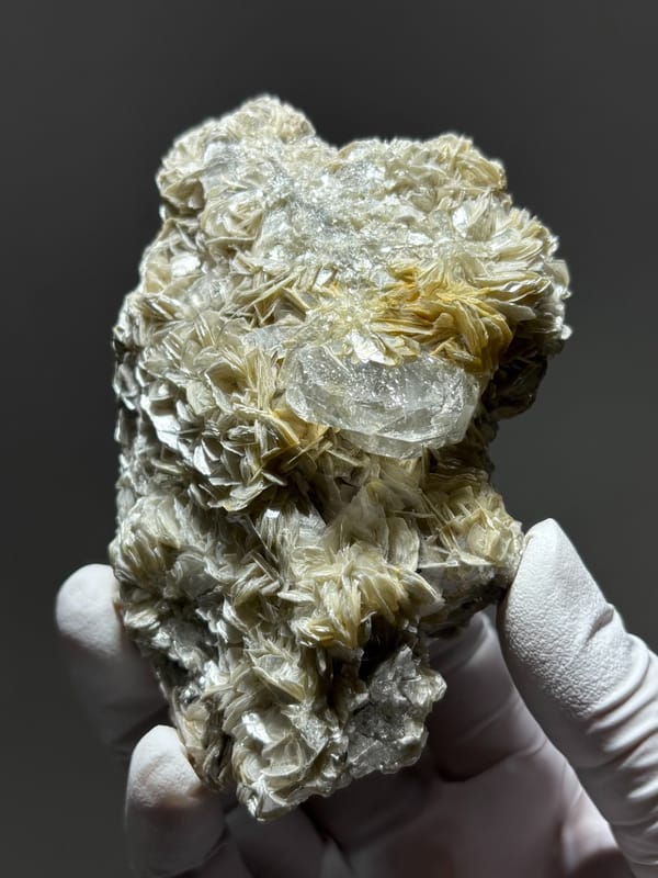 Pale aquamarine nestled in mica block from Xuebaoding, Sichuan, China, held in gloved hand