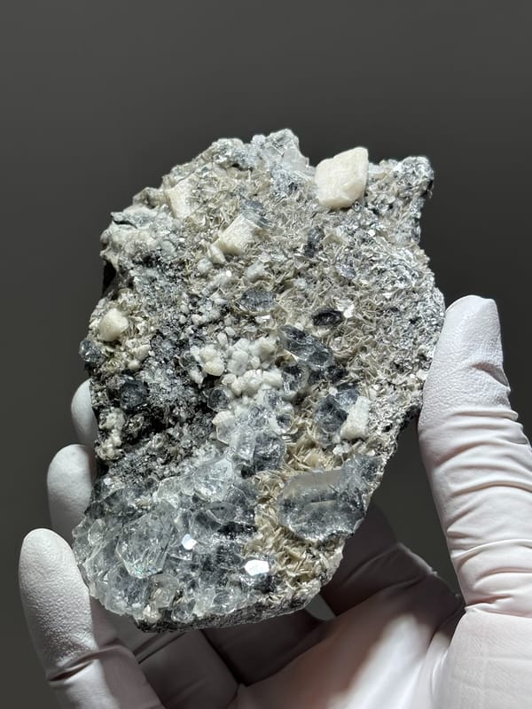 Grey plate with aquamarine, mica and feldspar from Xuebaoding, Sichuan, China, held in gloved hand