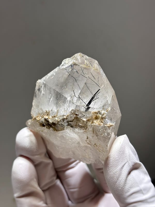 Clear quartz with jamesonite needles on mica from Xuebaoding, Sichuan, China, held in gloved hand