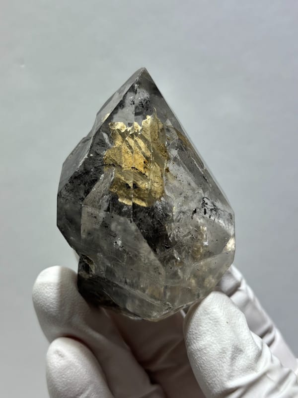 Clay skeletal quartz floater with rainbow flashes from Guizhou, China, held in gloved hand