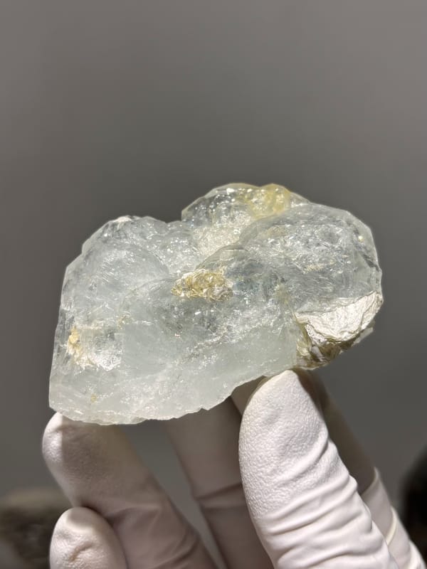 Pale green aquamarine block with golden patch from Xuebaoding, Sichuan, China, held in gloved hand