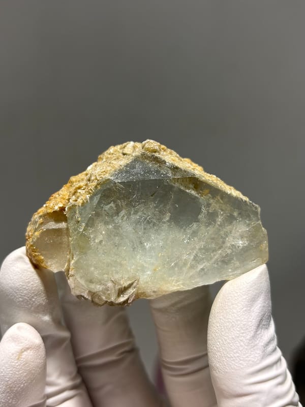 Flat pale green aquamarine with golden mica rim from Xuebaoding, Sichuan, China, held in gloved hand