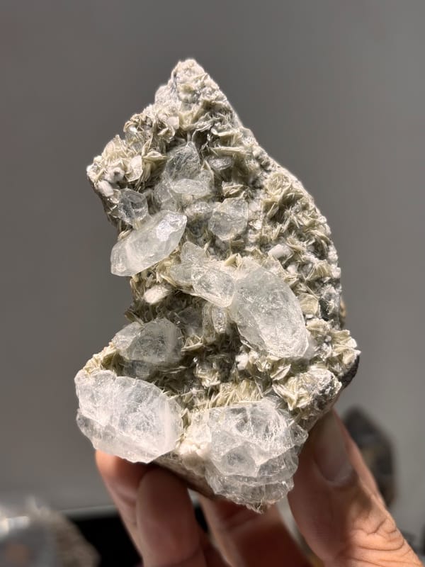 Grey mica plate with pale aquamarine crystals from Xuebaoding, Sichuan, China, held in hand