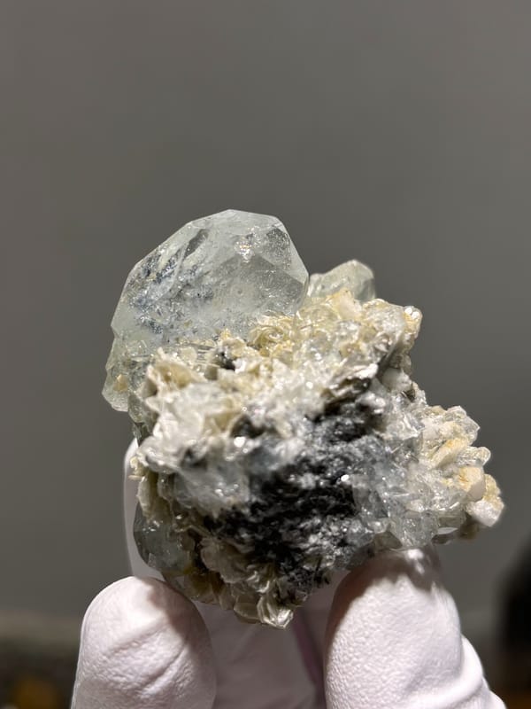 Pale blue aquamarine over white mica and feldspar from Xuebaoding, Sichuan, China, held in gloved hand