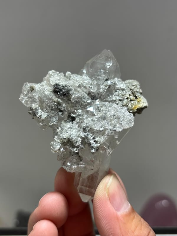 Clear quartz cluster with mica and dark flecks from Xuebaoding, Sichuan, China, held in hand